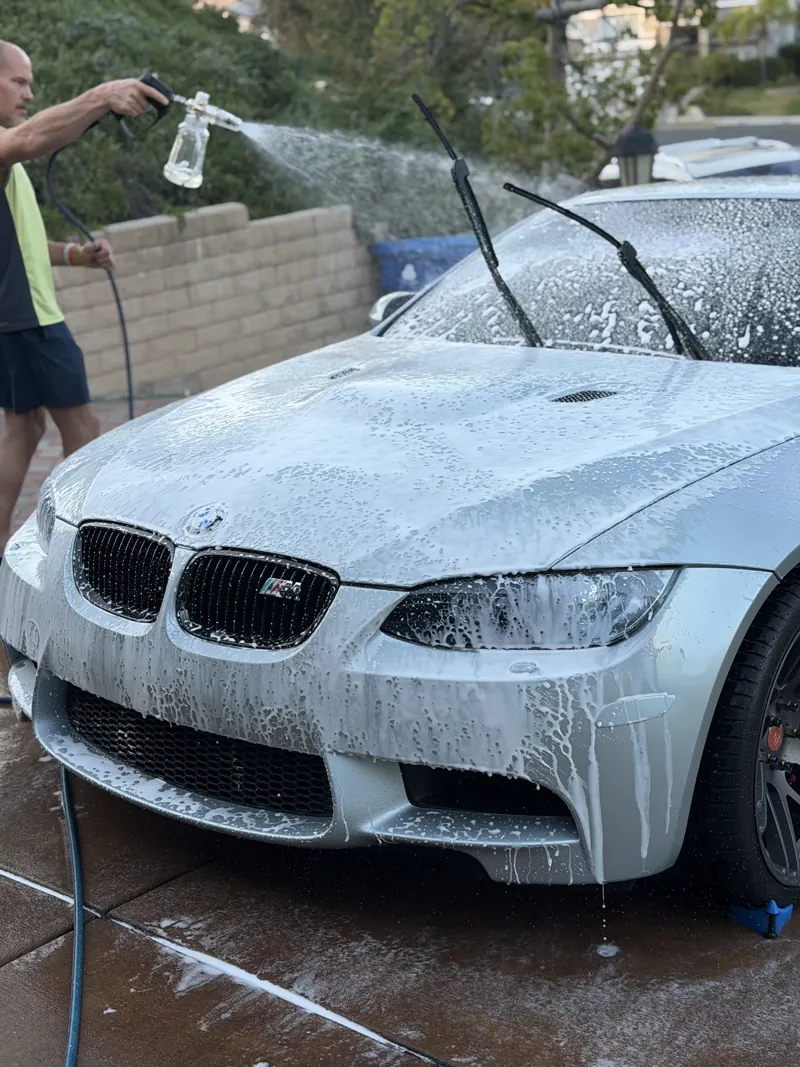 Detailer foaming a silver BMW M3 in a residential driveway